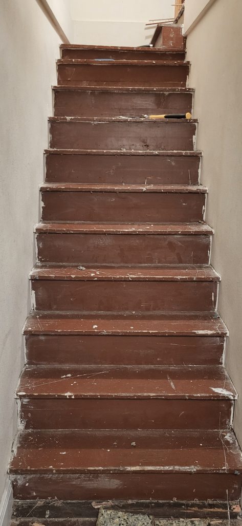 Carpet removed from stairs. Bare wood stairs. Dark stairwell before paint