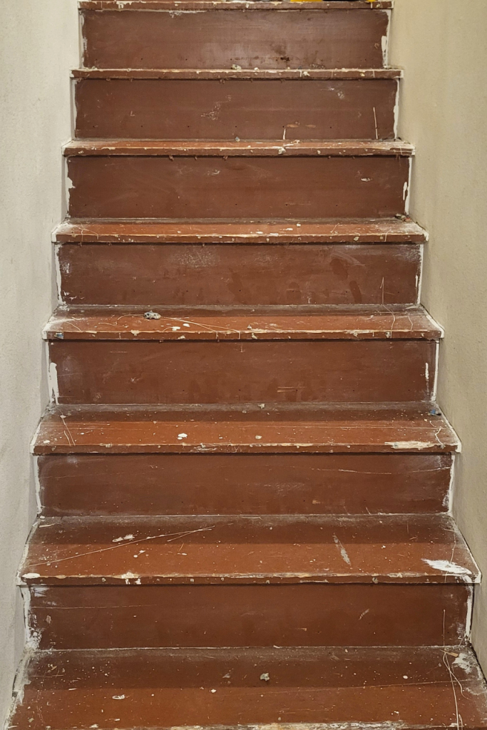 Stairwell after removing the carpet, showing worn brown-painted wood treads with scratches, holes, and old staple marks before the makeover.