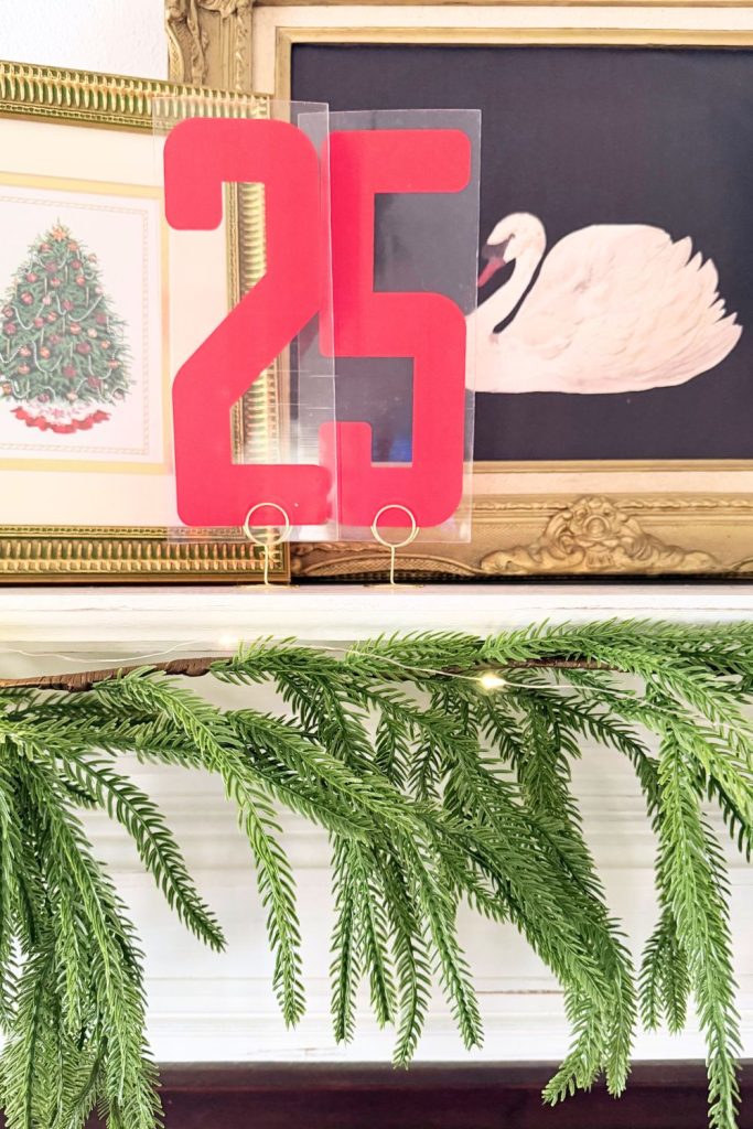 Bright red marquee number “25” displayed above a vintage gold frame with layered greenery garland for festive farmhouse Christmas mantel decor.