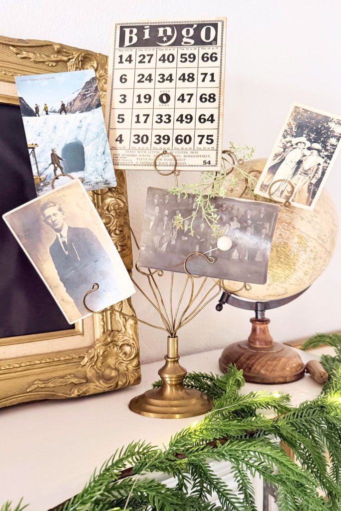 Vintage vignette featuring brass photo holder, antique globe, old family photographs, and gold picture frame styled with greenery for a collected farmhouse look.