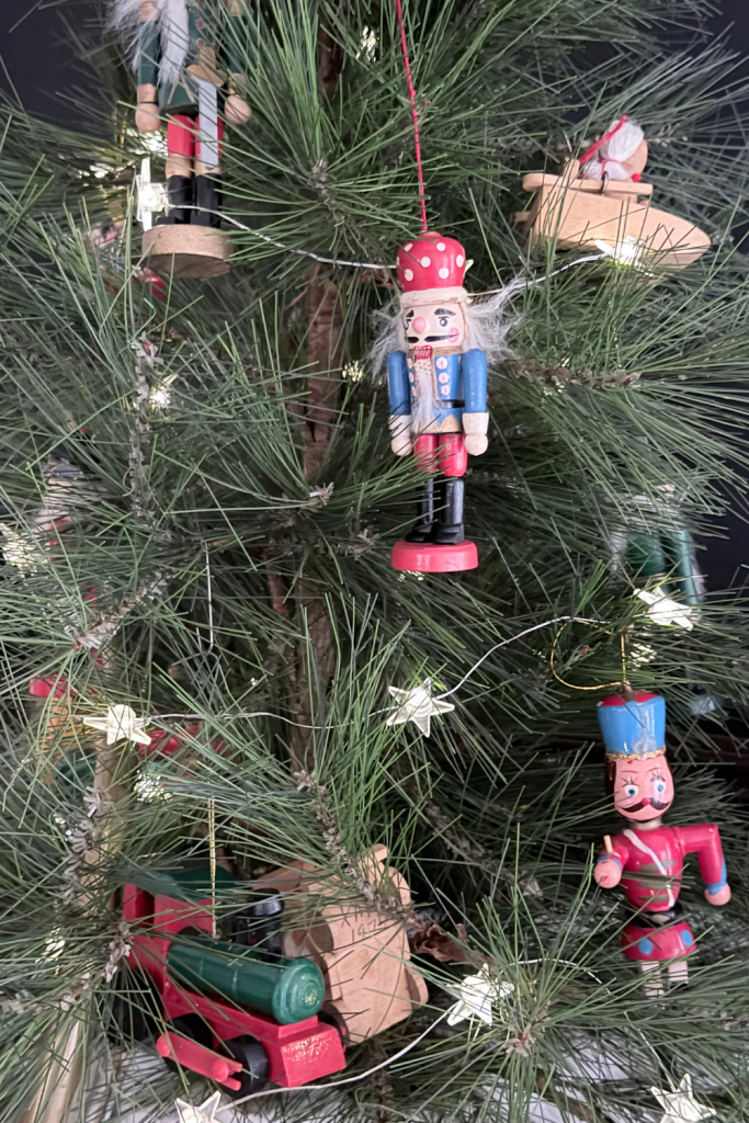 Close-up of a tabletop Christmas tree decorated with vintage nutcracker ornaments, knitted red-and-white stocking garland, and nostalgic holiday accents on a dark chalkboard backdrop.