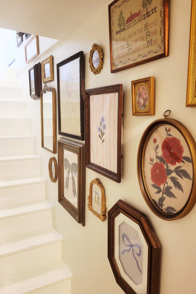 Thrifted vintage wall decor featuring framed artwork and crewel embroidery displayed on a stairway wall