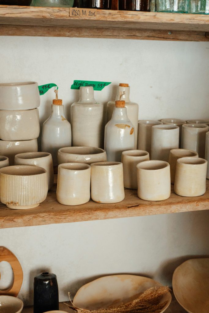 Neutral handmade ceramic cups and bottles displayed on rustic wooden open shelving, creating a warm English cottage–style kitchen look.
